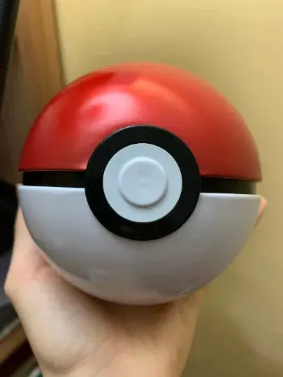 Hand holding a classic red and white Pokémon Poké Ball collectible toy from PTC Collectibles
